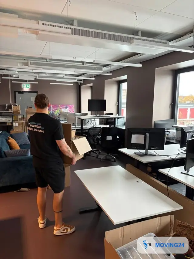 Сотрудник Moving24 несёт коробку в офисе открытой планировки